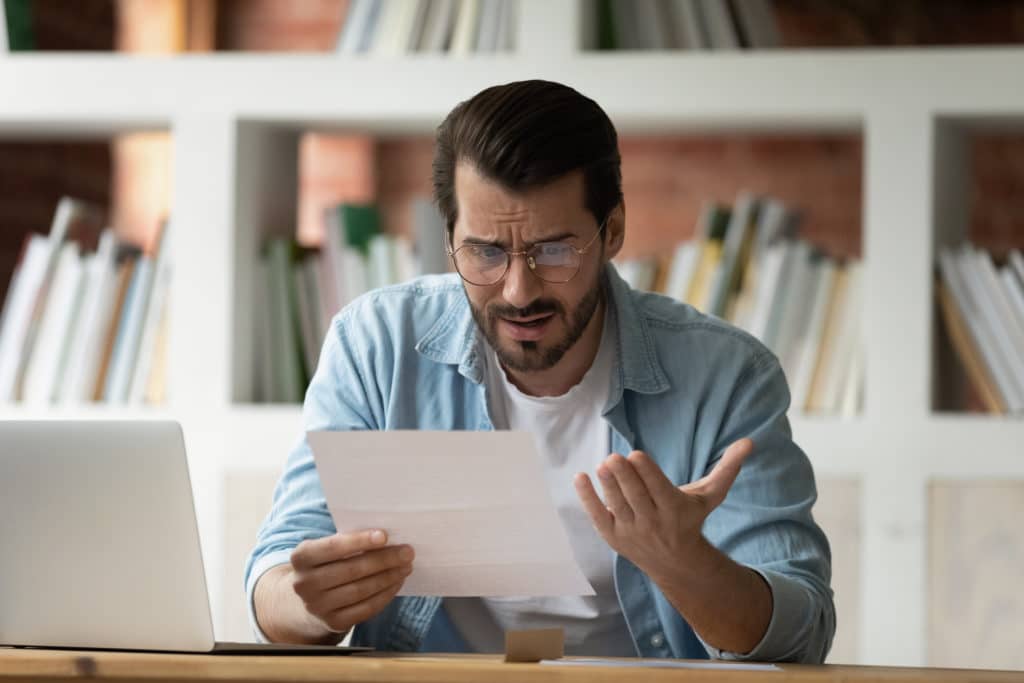 Young man holding paper letter reading shocking unpleasant unexpected news