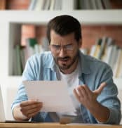 Young man holding paper letter reading shocking unpleasant unexpected news