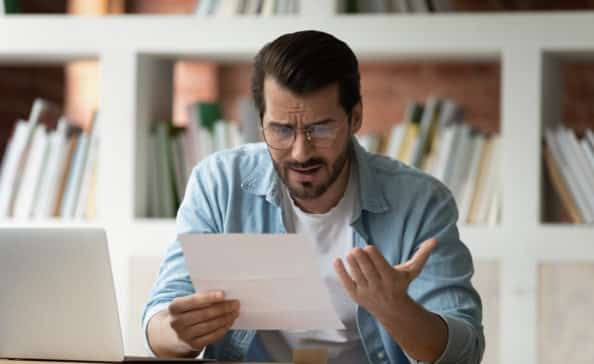 Young man holding paper letter reading shocking unpleasant unexpected news